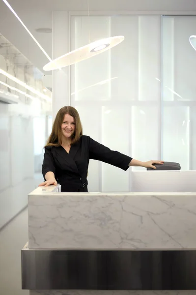 Genç bir kadın, beyaz ışık ofis hastanesi diş hekimliği resepsiyonunda bilgisayarın başında oturuyor. Uzun saçlı, siyah giysili, beyaz dizüstü bilgisayarlar.