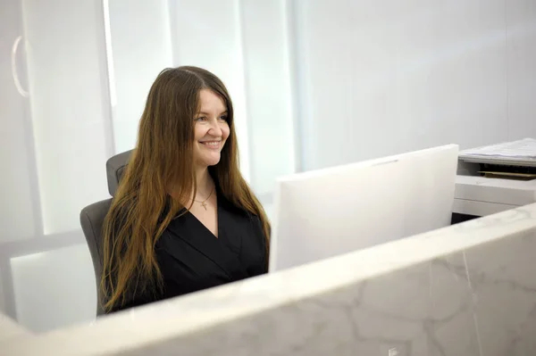 stock image A young woman sits at a computer at the reception of a white light office hospital dentistry any computer programmers long hair black clothes white computer laptop