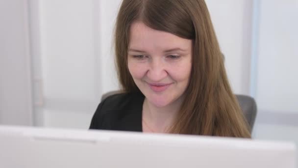 若い女性は白いライトオフィス病院歯科の受信時にコンピュータに座っている任意のコンピュータプログラマー長い髪黒の服白いコンピュータのラップトップ — ストック動画