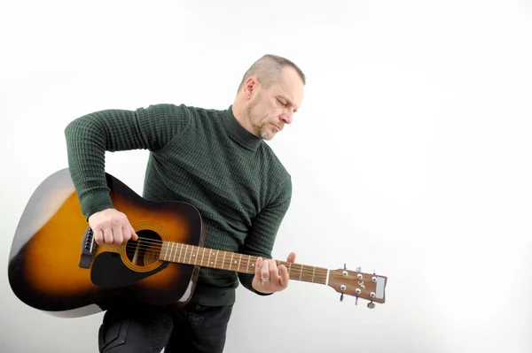 Music melody under the verses adult confident man playing the guitar on white background in the studio green sweater golf under the neck beard and mustache jeans