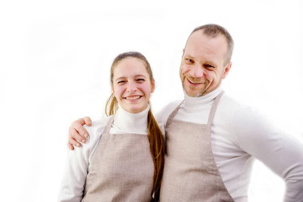 master and apprentice smile and look into frame chef and assistant father and daughter on a white background two people beige kitchen or technical aprons sincere smile warm relationship joy ad