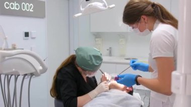 Diş hekimliği, yirmilik diş çıkarma, diş hekimi ve asistan diş kökü cerrahi eldiveni, beyaz diş hekimliği en son teknolojiyi çıkarmaya çalışırken hasta aletleri üzerine eğildi.