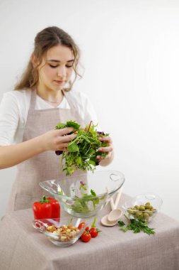 girl mixes lettuce with hands she pours it into glass plate vegetarian food healthy food wooden spoons apron tablecloth young woman teenager prepares dinner for family dinner breakfast lunch