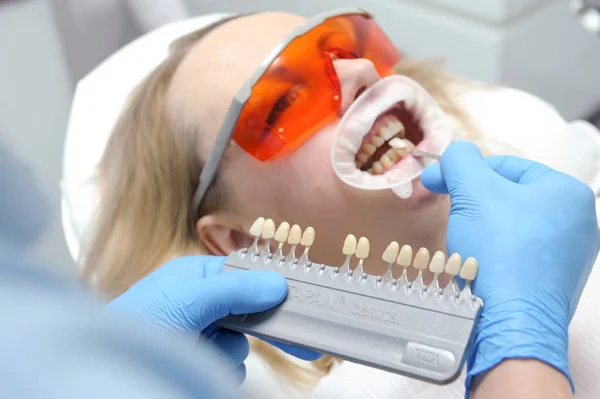 classical dental coloring for determining color of teeth dental clinic using optragate mouth dilator woman getting teeth color matched after whitening close-up face in uv protection goggles