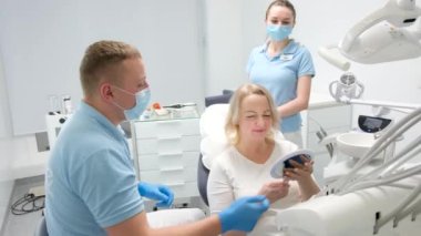 classical dental coloring for determining color of teeth dental clinic doctor hands over mirrors middle aged woman patient she is happy with result smiles shows thumbs up laughs and gives mirror