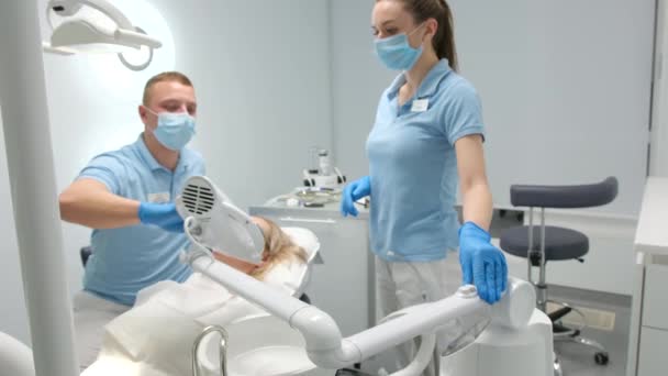 歯科医院最先端技術患者医師と看護師歯を白くする医師が機械を拾うと看護師は特別な技術を脇に置きますUv保護ゴーグル — ストック動画