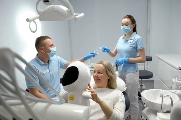 dental clinic middle aged woman sitting in chair with astronaut soft toy smiling pretty showing child that it is safe to sit fear of dentistry children nurse handing goggles to doctor
