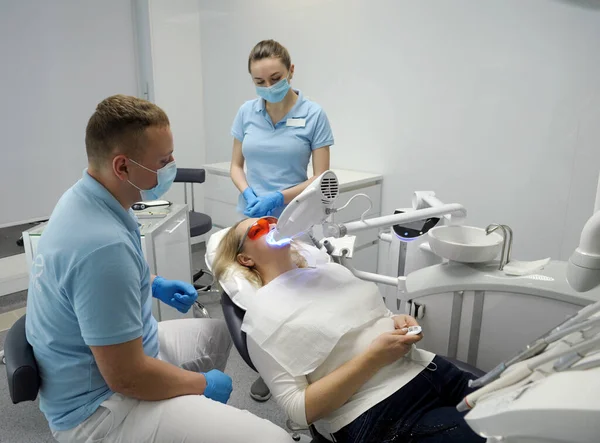 dental clinic teeth whitening woman lying under apparatus doctor and nurse watching waiting for completion of process in womans hands holding panic button to call doctors Beyond Poluse Plus