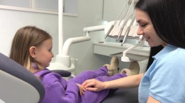 hold the hand, be afraid of the dentist Lovely little kid smiling while talking with the pediatric dentist after doing a tenth examination in a pediatric stomatology cute little girl sits dental chair