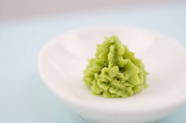 Green wasabi sauce or paste in bowl, with chopsticks or spoon over plain colourful background. selective focus . High quality photo