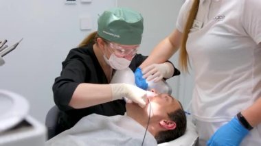 Take a picture with a portable x-ray Female doctor dentist is showing x-ray teeth on tablet to young female patient. Dentist is wearing lab coat. High quality 4k footage