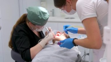 The dentist and his assistant treat the patient. Dental treatment in modern dentistry. A close-up shot of patient in a dental chair undergoing a tooth extraction procedure. Medicine and healthcare 4k