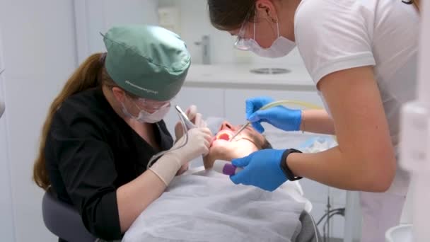 歯医者と助手は患者を治療する 現代の歯科における歯科治療 歯の抽出手順を受けて歯科椅子で患者のクローズアップショット 医学と医療 — ストック動画