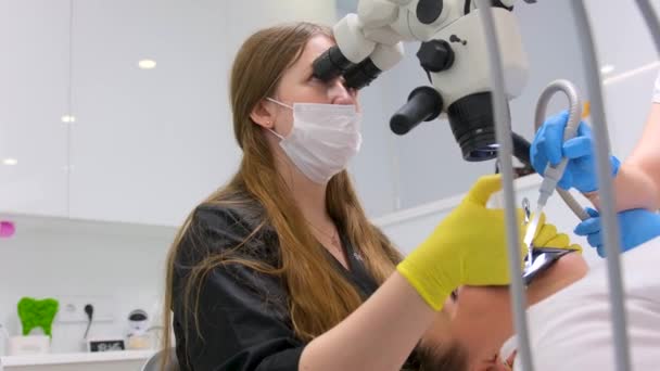 在诊所办公室使用现代牙科显微镜对病人进行口罩口罩检查的女牙医 在场的女性医务助理 高质量的4K镜头 — 图库视频影像