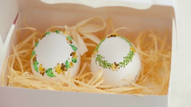 白い箱の中の卵のための休日のイースター刺繍のためのテキストバナーのポストカード招待状のための卵殻の場所透明なオープントップと白い背景の箱の上に小麦の3つのスパイク — ストック動画