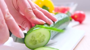 female hands close-up cutting cucumber on a white porcelain board in round circles with rings cooking application on the eyes cooking salad