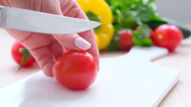 female hands cut cherry tomatoes on a white cutting board knife cuts tomato half delicious tomato juice flows out in vegetables yellow bell pepper cilantro cucumbers cooking salad slicing vegetables