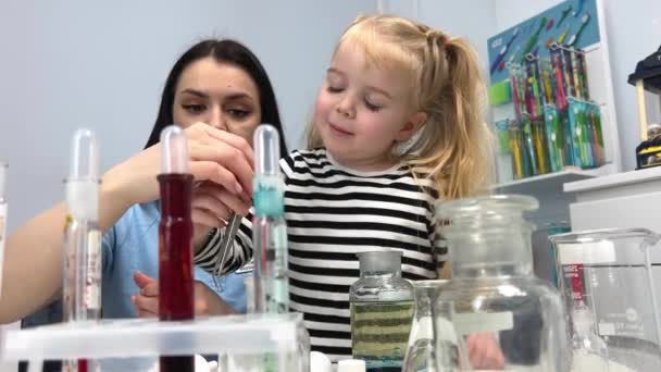 实验室儿童化学实验快乐的女孩拿出玻璃瓶中的石碑 在附近的实验室助理微笑着 边看边帮助小女孩 — 图库视频影像