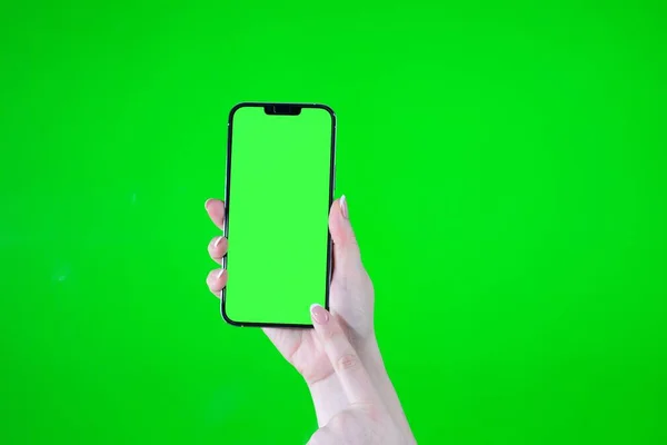 in female hands a green screen in the phone on a green background with other hand points to the lower right corner