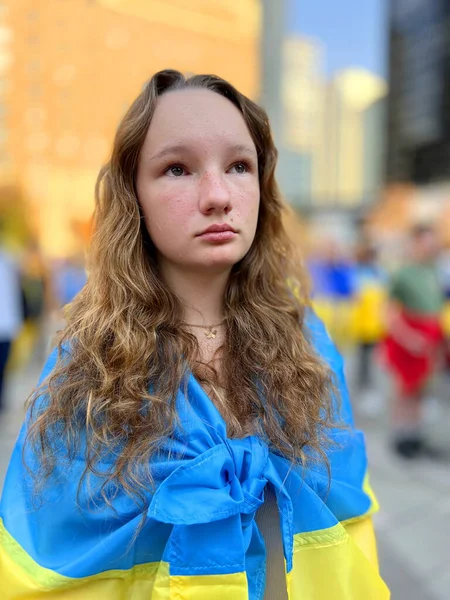 young beautiful sad girl teenager stands at rally against war we are for peace No war girl on shoulders with flag of Ukraine raised her eyes up and wants peace waiting for the end of the war emigrants