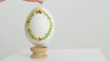 close-up of an embroidered egg on the eggshell of goose eggs female hand slowly puts it on a wooden stand on white background krashenka drawings ornaments scenery easter celebration