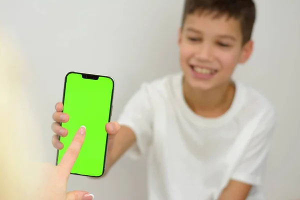 happy boyshowing phone with green screen to woman she chooses place of your advertisement with her finger on white background online store childs joy purchase gift celebration Interesting game