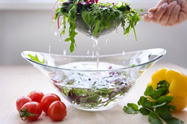 A woman chef in a striped apron is is tearing freshly washed, fresh, clean leaves of lettuce into a separate glass bowl. She is located in a rustic style kitchen. High quality photo