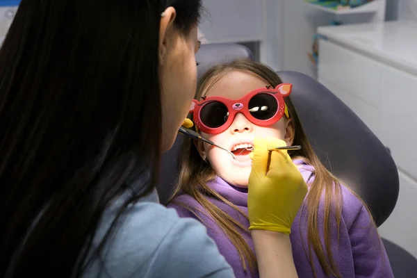 pediatric dentistry close-up little girl opened mouth shows teeth doctor looks at whether she has caries fillings treatment examination by doctor girl wears red sunglasses so that dental lamp