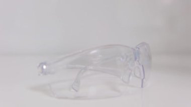 Close up of protective eyeglasses lying on desk in dental office. Dentists glasses on desk. Close-up womans hand takes dentists glasses