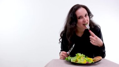 on white background woman in black clothes eats a salad and meat with fork looks into the frame space for text proper nutrition white background one woman tasteless food forced diet