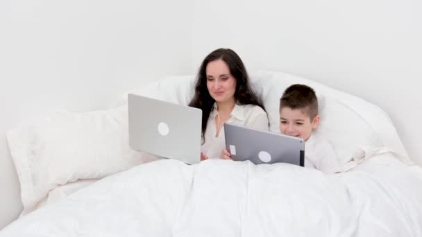 在家里上网的女人在毛毯下工作在笔记本电脑旁和儿子一起在家里玩平板电脑生病的游戏家庭隔离检疫白纸绒毛妈妈和儿子 — 图库视频影像