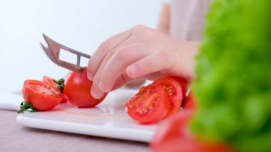 preparing healthy vegetable salad on cutting board in restaurant kitchen. Concept new lean menu close-up of the hands of the child and mother cut cherry tomatoes on a white porcelain board