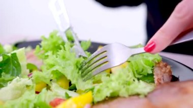 A girl eats vegetable salad with a fork from a white plate. Close up shot. High quality 4k footage