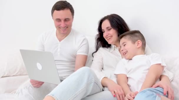 在床上玩平板电脑的家庭诚挚的笑着妈妈和儿子玩的开心爸爸和儿子乌黑的头发白色的大绒毛家庭和儿子一起在笔记本电脑上看电影很好的打发时间进行检疫 — 图库视频影像