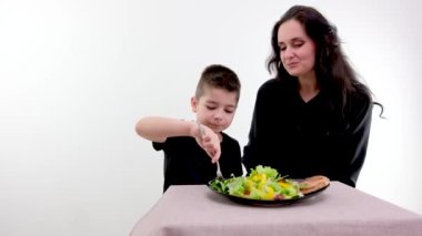 mom and son in black clothes at table boy feeds mom with vegetable salad care helping parents learn to eat with fork pleasure of communicating with children salad and meat on black plate laughter joy