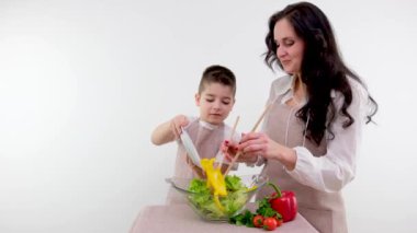 Anne oğluna salata pişirmeyi öğretiyor. Cam tabağa sarı biber ekliyor. Yemek yapmayı öğreniyor.