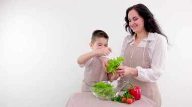 Anne ve oğlu salatayı elleriyle hazırlıyorlar. Marul, beyaz arka plan boşluğunu mesaj atmak için bırakıyor. Çocuğa yemek pişirmeyi öğretiyor.