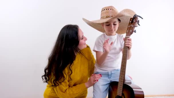 Mamá Hijo Fondo Blanco Estudio Niño Toca Guitarra Enorme Sombrero — Vídeo de stock