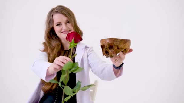 医学治療回復疾患薬広告製品技術現代医学白い衣と赤いバラと人間の頭蓋骨と白い背景に黒いセクシーな服の美しい女性 — ストック動画