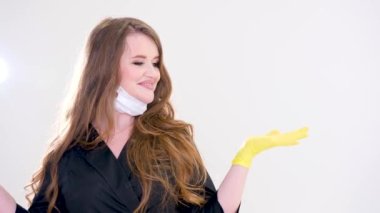 female doctor in a black suit with flowing hair with a mask lowered to her chin points with her hand to an empty space for advertising text yellow and blue hygienic glove studio white background