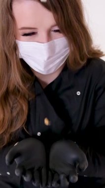 dentist in black clothes and black gloves holds hands on which wisdom teeth of real people are pouring out pulling out tooth extracting woman looks into frame on face mask blinks eyes does not take