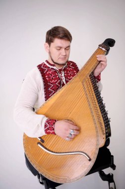 strong Ukrainian Cossack in an embroidered shirt Red cross-stitch on a white linen leaned on a musical instrument bandura and looks into distance with sad look confidence strength of courage hero