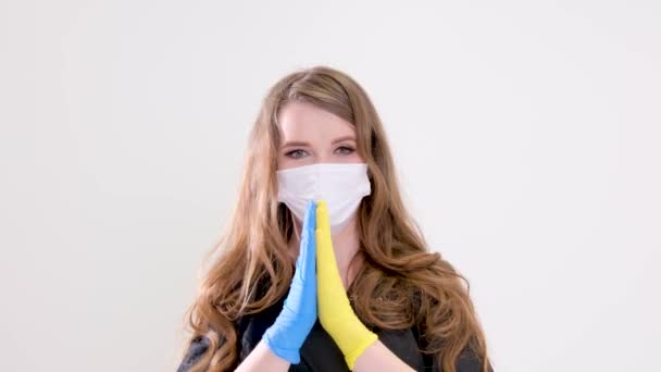 ウクライナの女性医師のために祈ることができます彼女は手を伸ばす白い背景スタジオでマスクと顔の近くにウクライナの国旗のようにラテックス手袋黄色と青で2つの手を折るヘルプのための愛の呼び出し — ストック動画