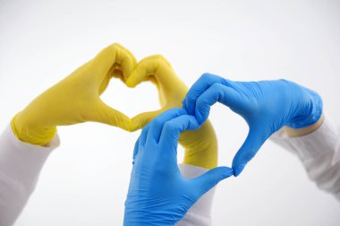 hands of two nurses make a heart in the air on a white background blue and yellow latex gloves understanding help mutual assistance Hippocratic oath help patient love of life cardiology protect heart