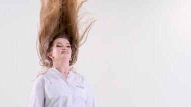beautiful female doctor on white background in studio raises head hair flying wave head loose hair after working day rest relaxation take off a headdress vacation end of work end of working day