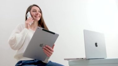 new technologies Apple MacBook 14 pro phone iPhone 13 pro Max and iPad on white background the girl uses all the latest technologies talking on the phone smiling holding a tablet looking at a laptop