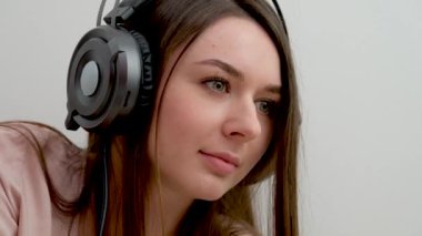 close-up face of girl in headphones on white background studio near laptop slow motion video close look beautiful young face cute woman freelance work as musician social help communication