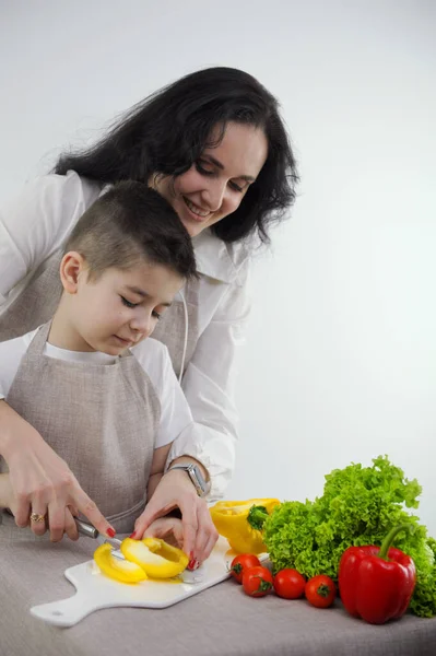 cooking courses for children mom teaches to cut vegetables with knife yellow bell pepper finely chopped into strips in family at home white background apron kitchen vegetables lettuce leaves