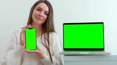 Be H3althy beautiful tender girl in a white jacket distributor seller shows a phone with a green screen she scratches her chin straightens her hair smiles looks into the frame chroma key green monitor
