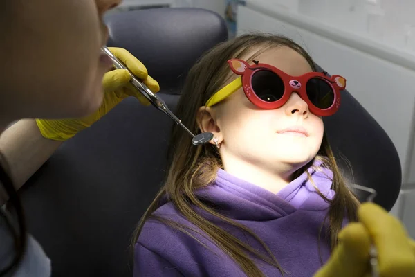 pediatric dentistry girl is afraid of doctor turns head away doctor tries to persuade to have dental procedures first visit to doctor sit in chair dentist yellow latex gloves lilac tracksuit of girl